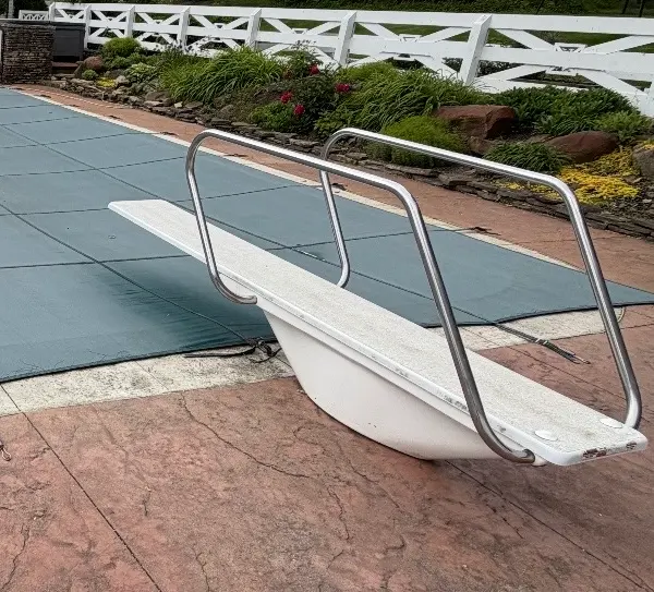 Covered in-ground pool with a diving board and a stamped concrete deck