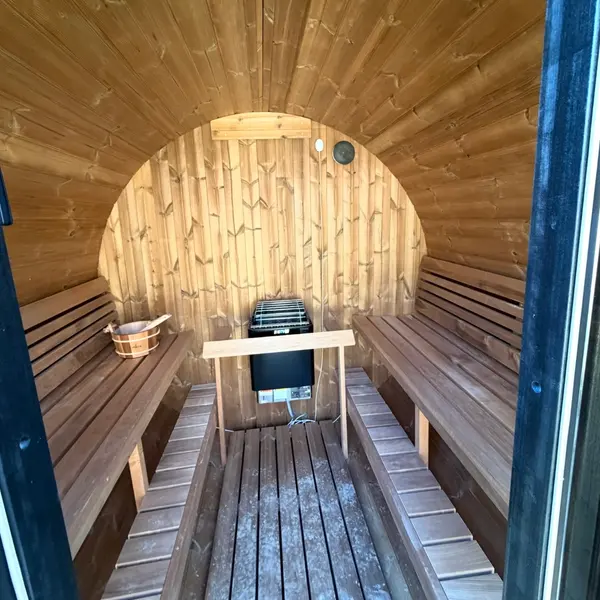 Inside a cedar barrel sauna with the electric heater wired and mounted between the benches