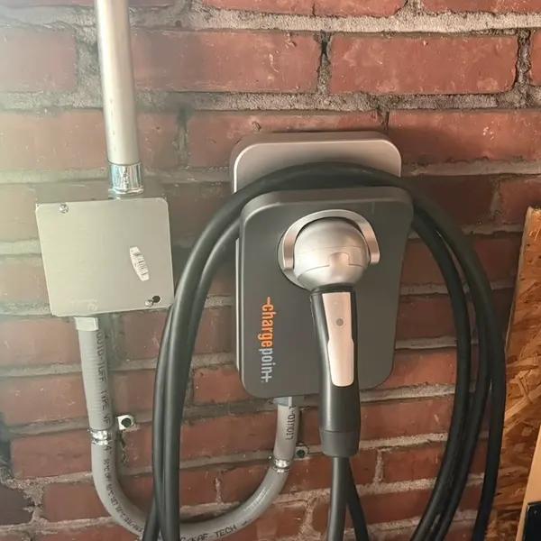 Level 2 EV charger mounted on a brick garage wall, fed through rigid conduit and a junction box