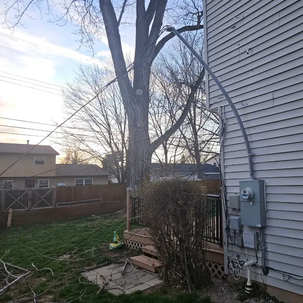 Service mast bent over on the side of a house with the service drop hanging slack after a storm, before repair
